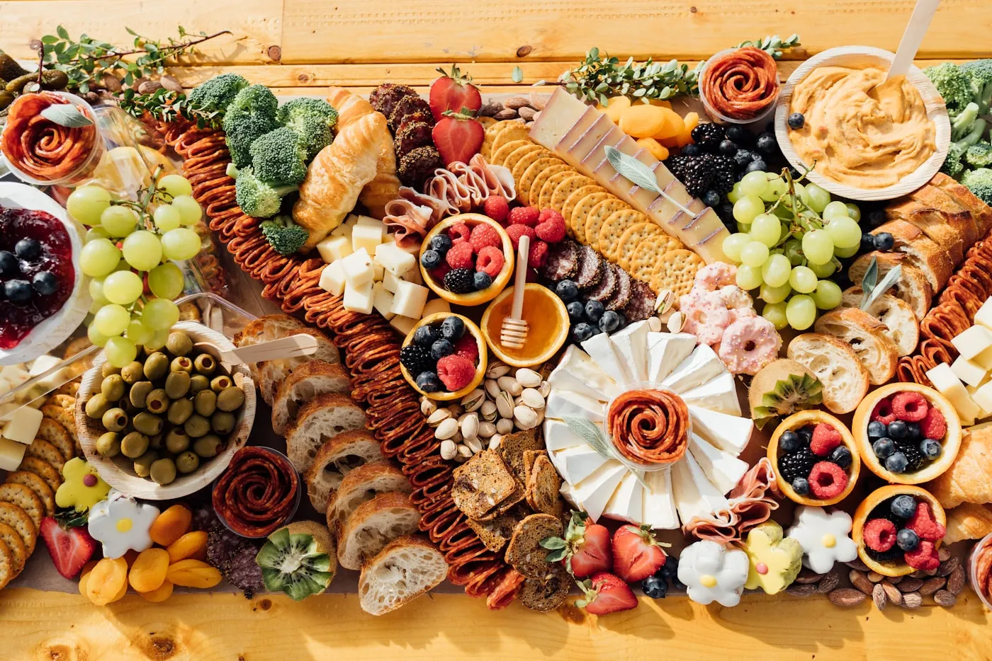An abundant grazing table topped with cheeses, cured meats, crackers, fruit, and dips on wood.